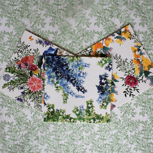 Three flower illustrated square cards on a green printed tissue paper background.