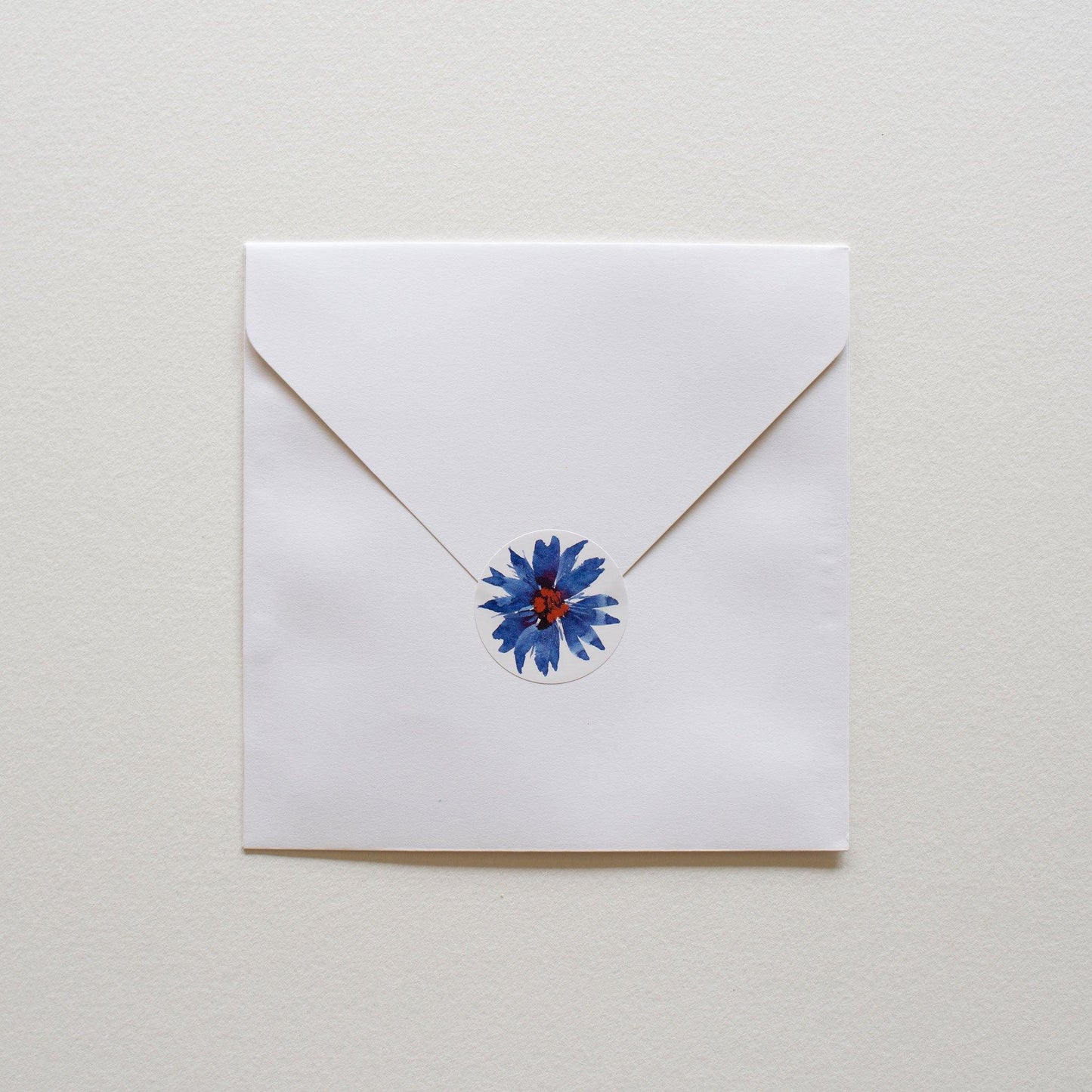 Square white envelope with round illustrated sticker to close.