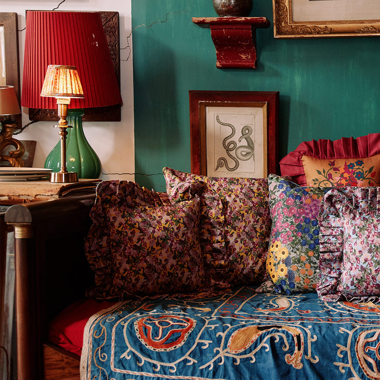 Colorful pillows stacked on a day bed, with a side lamp with pleated lampshade