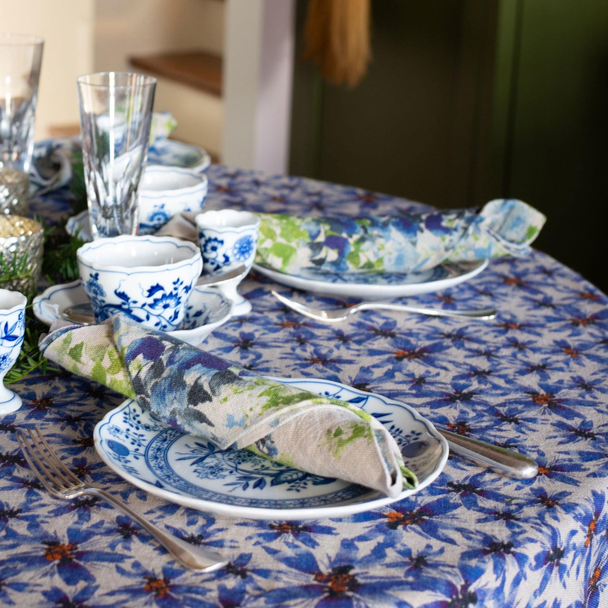 Blue flower printed linen table cloth setting with blue and white china and blue and green linen napkin.