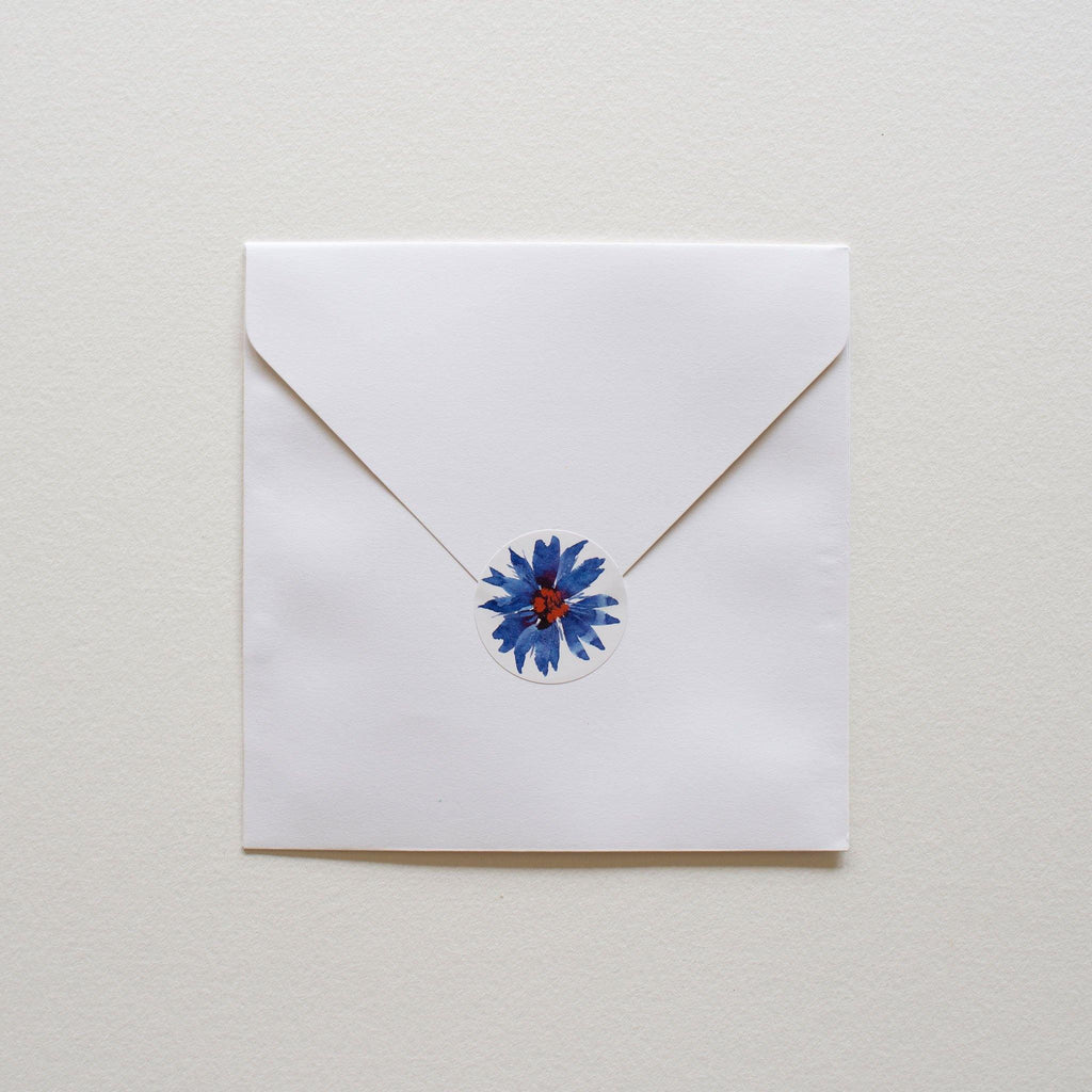 Square white envelope with round illustrated sticker to close.