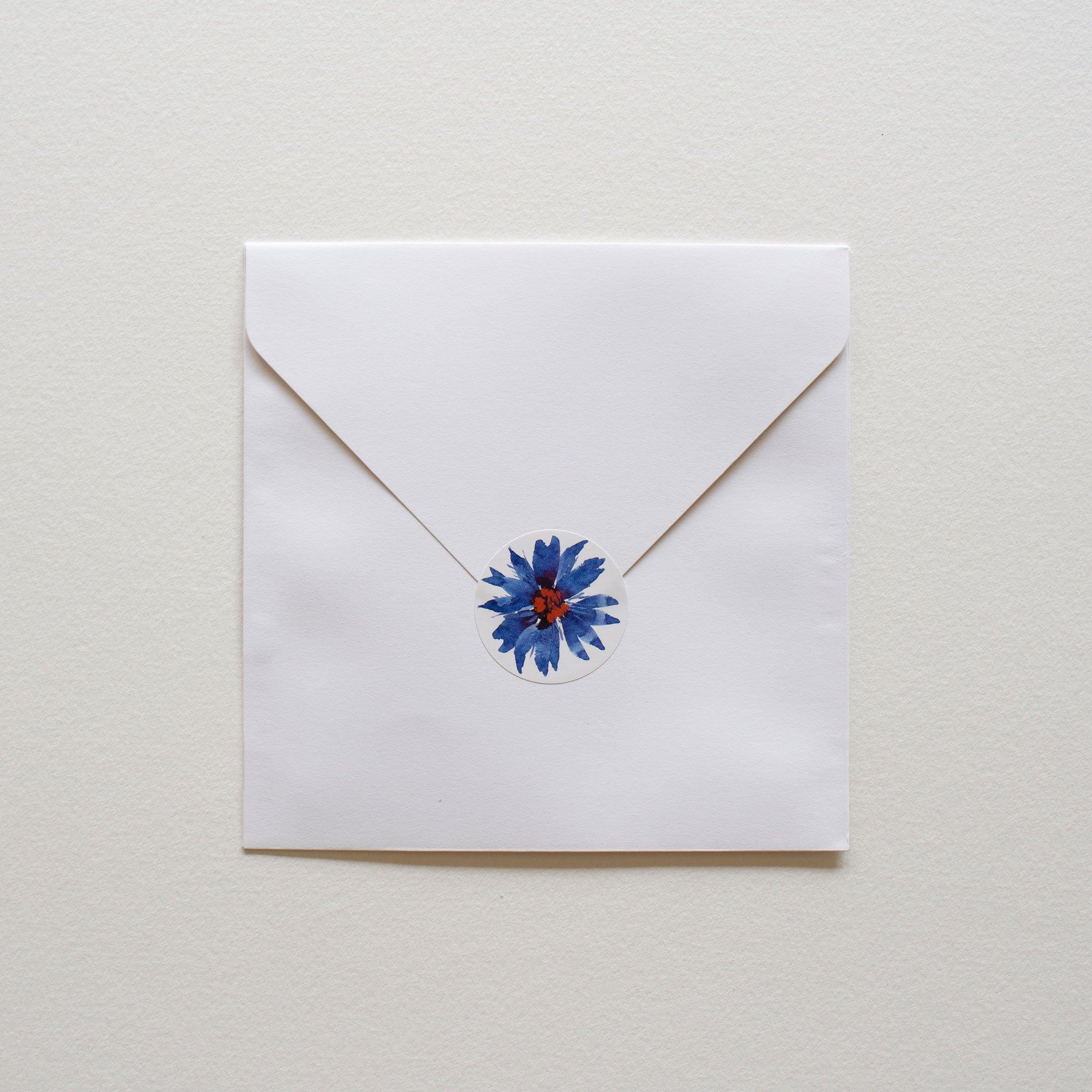 Square white envelope with round illustrated sticker to close.