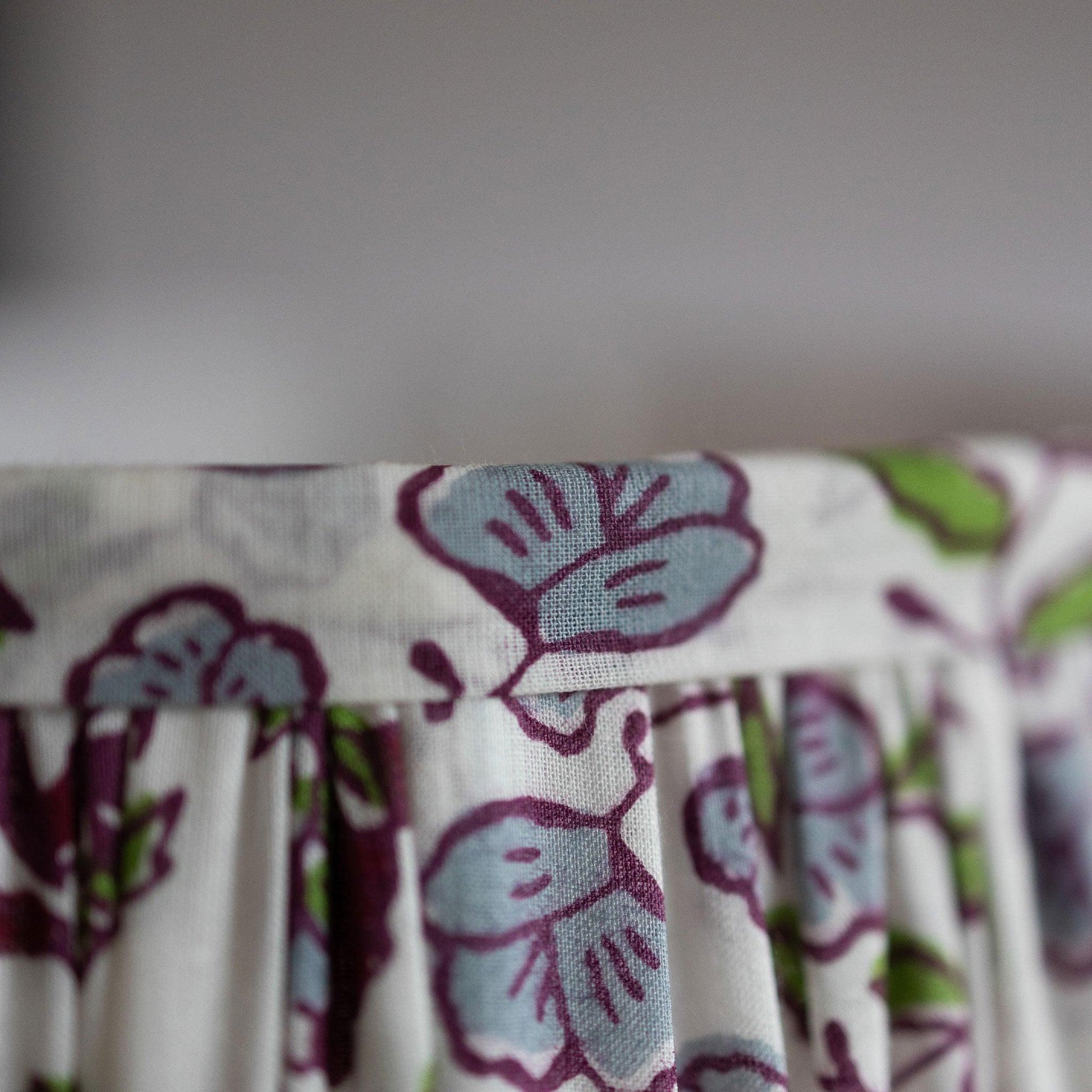 Closeup detail of border of hand block printed organic cotton in plum, green, purple and white lotus motif.