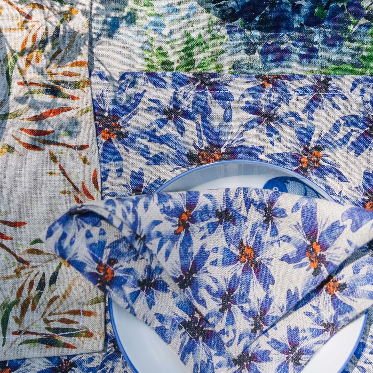 Close up of a rectangular placemat and napkin made of organic linen and ethically produced in India, printed with blue cornflowers and orange blossoms, designed by Sophie Williamson Design