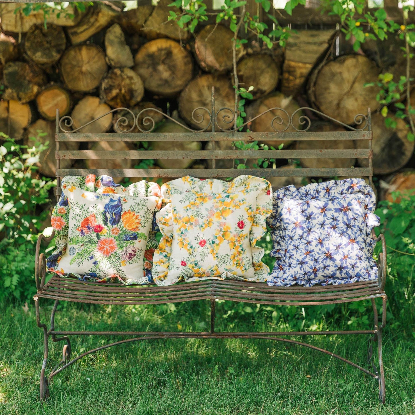 Three ruffled pillows printed with bright florals on an outdoor bench in a romantic setting.