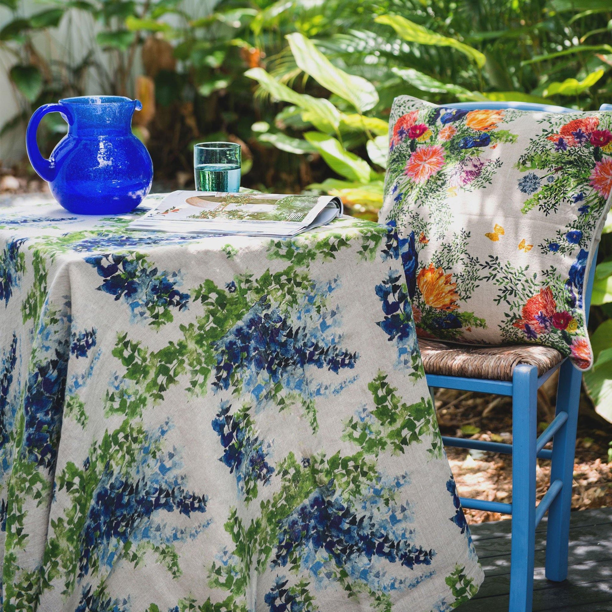 Outdoor table scene with blue and green linen table cloth and colorful floral print cushion
