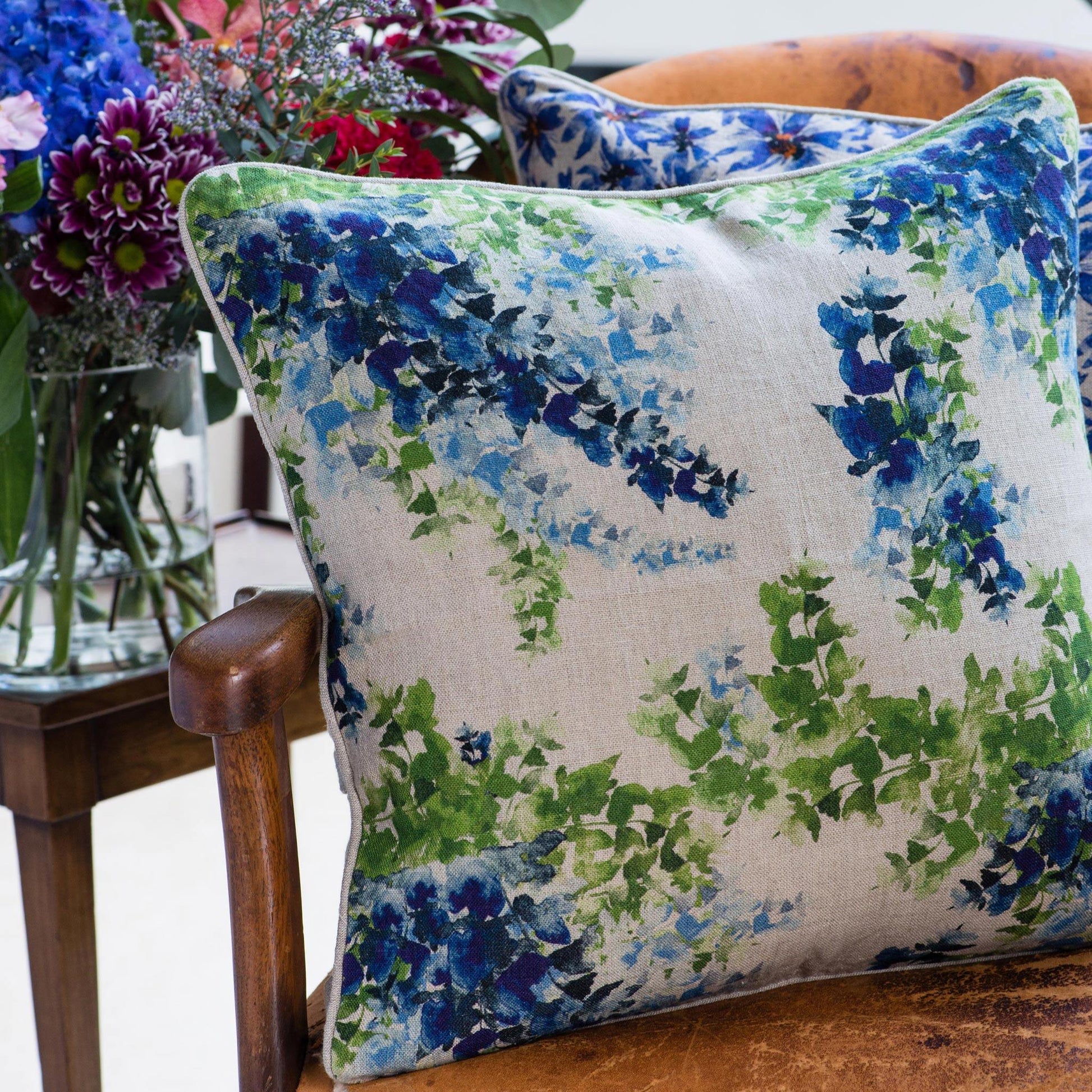 Blue and green floral print organic linen pillow cover on leather chair with flowers in background.